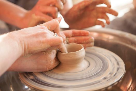 Unrecognizable potter showing students how to throw pot on potters wheel