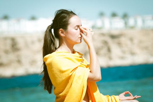 young woman doing yoga breathing pranayama at the blue sea bakcground