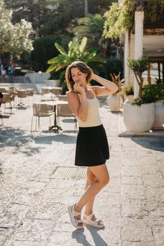 Girl tourist walking through ancient narrow street on a beautiful summer day in MEDITERRANEAN MEDIEVAL CITY , OLD TOWN bUDVA, MONTENEGRO. Young beautiful cheerful woman walking on old street at tropical town. Pretty girl looking at you and smiling