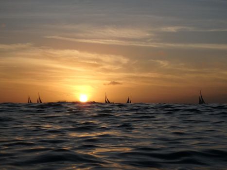 Dramatic Sunset on waters of Waikiki over the ocean with sail boats on the horizon on Oahu, Hawaii.