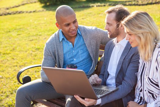 Group of business people enjoying working outdoors together, using laptop at the park