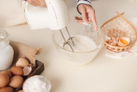 Male hands beating egg whites cream with mixer in the bowl