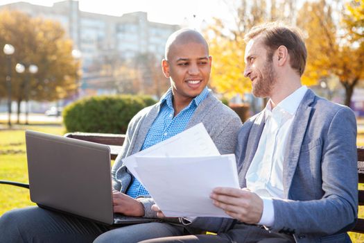Two business colleagues chatting outdoors in the park. Handsome African American male entrepreneur enjoying working outdoors with his business partner