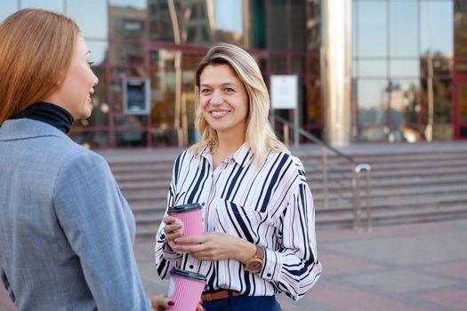 Mature businesswoman having coffee with her colleague outdoors. Two female entrepreneurs having coffee break during working day