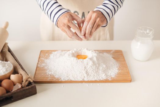 Egg poured into flour during the baking process, man's hands
