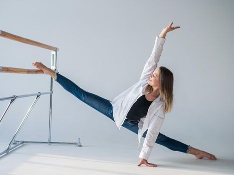 Caucasian woman in casual clothes pulls the split at the ballet barre