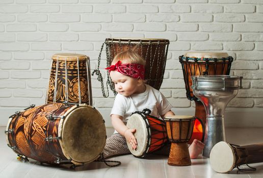 Cute toddler baby playing ethnic drums next to bricks wall