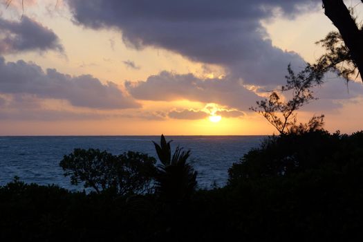 Early Morning Sunrise through the trees over an island and ocean on Waimanalo Beach on Oahu, Hawaii with clouds hanging in the air.