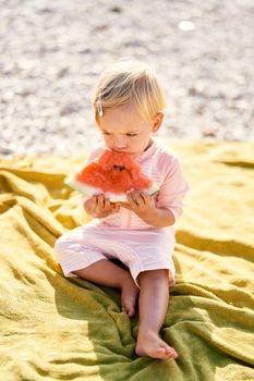 Little girl eats watermelon on a blanket on a pebble beach. High quality photo