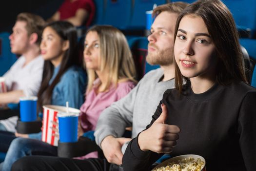 Best friends time. Beautiful brunette showing thumbs up while enjoying movies with her friends at the local movie theatre