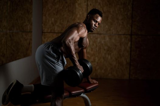 African american man with naked torso doing triceps row with dumbbell on bench