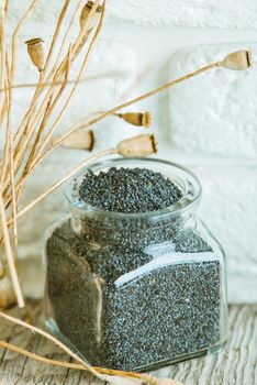 poppy seed in glass with dryed flowers plant on wooden board