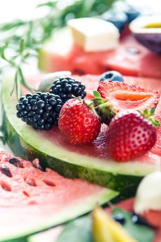 variation of summer berries and fruits cutted in pieces on white wooden background