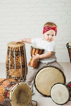 Cute toddler baby playing ethnic drums next to bricks wall