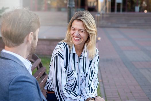 Beautiful mature businesswoman laughing, talking to her colleague outdoors in the business city, copy space. Communication, success concept