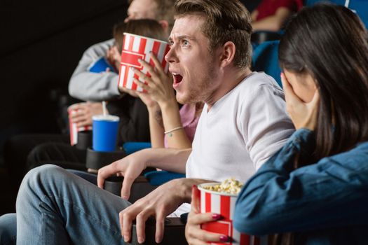 Good lord! Young man looking extremely shocked watching scary movies with the group of his friends at the local movie theatre