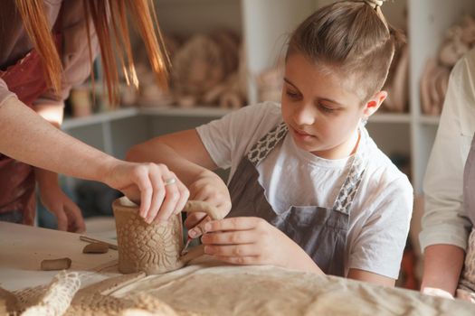 Close up of a young boy making ceramic mug with help of professional potter at art studio