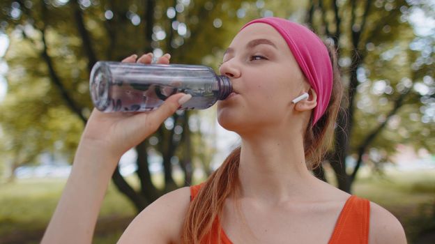 Athletic thirsty sport jogger girl drinking water from bottle after training exercising. Workout cardio in park at morning. Young woman runner enjoy healthy lifestyle. Active sportswoman activities