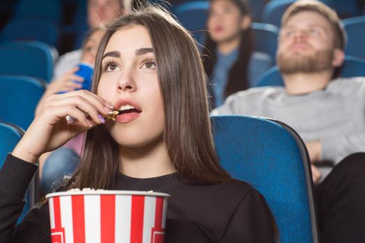 Perfect movie snack. Attractive brunette female eating popcorn while watching movies at the local movie theatre
