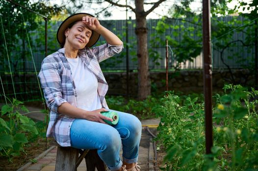 A pleasant Caucasian woman, farmer amateur with a tomato garter rope, enjoys gardening in her own organic vegetable garden. Eco farming, agricultural hobby concept. Cultivation homegrown vegetables.