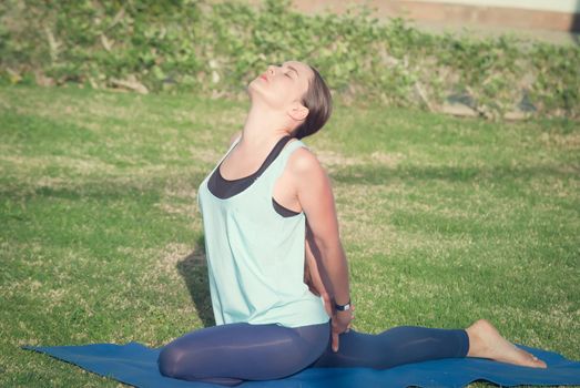 Young woman doing yoga at green grass in the park in the morning