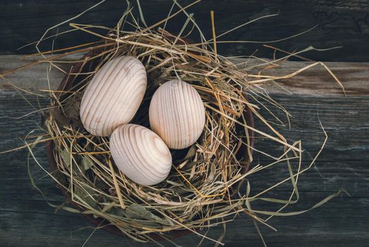 Easter decoration with wooden eggs in bascket and straw on wooden background