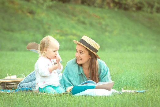 Mother is reading book for baby girl lying on the grass in the park. High quality photo