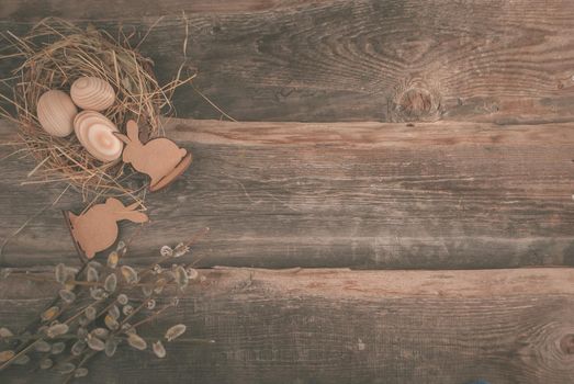 Easter decoration with wooden eggs in bascket and straw on wooden background