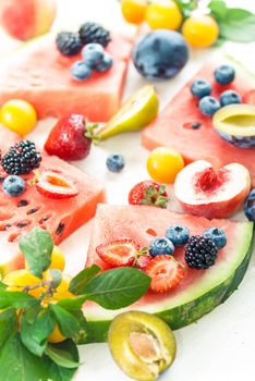 variation of summer berries and fruits cutted in pieces on white wooden background