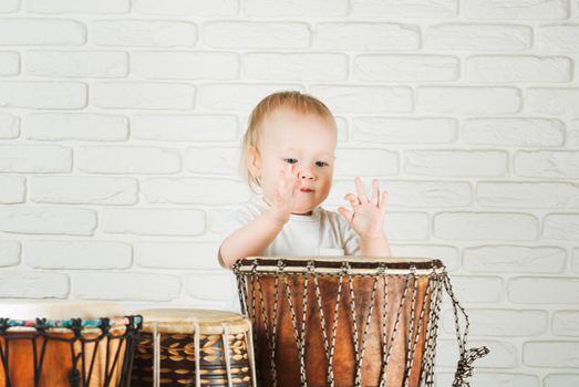 Cute toddler baby playing ethnic drums next to bricks wall