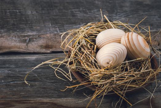 Easter decoration with wooden eggs in bascket and straw on wooden background