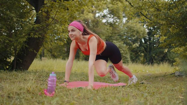Athletic sporty fit girl doing workout in park on sport mat performing training abs. Plank pose. Raises legs. Young woman enjoying exercising outdoors. Active sportswoman motivation. Weight loss