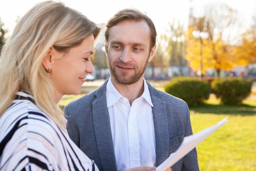 Mature businessman smiling at his female colleagues, while talking outdoors. Business colleagues talking outside on a warm autumn day