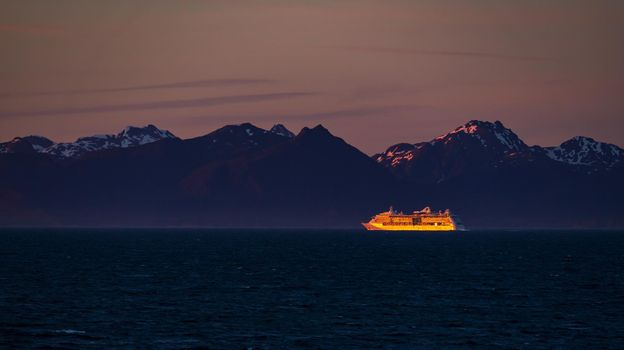 Late evening sunset illuminates a very distant cruise ship against the snowy Alaska coastline