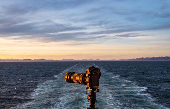 Professional dslr on tripod on back of cruise ship sailing away from Alaska coast leaving wake