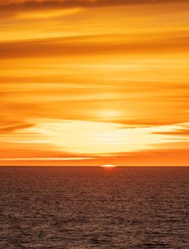 The final section of the sun drops below the water horizon with a colorful sunset over the ocean