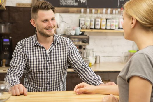 Cheerful barista talking to his female client at the coffee shop communication professionalism service restaurant bar cafe recreation lifestyle customer friendly profession occupation job worker working