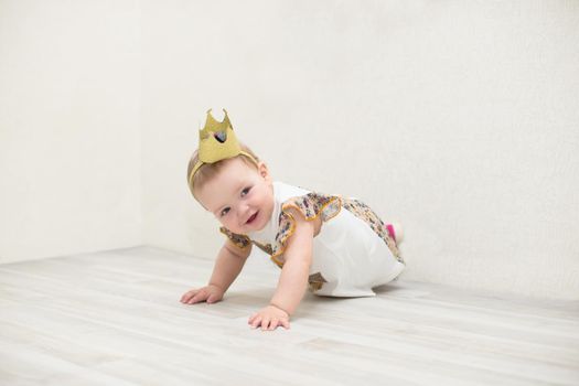 A one-year-old girl with a crown. The little princess crawls on the floor