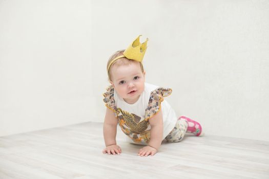A one-year-old girl with a crown. The little princess crawls on the floor