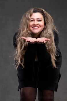 Beautiful fat woman with long curly hair and black dress blowing on her arms.