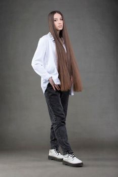 A beautiful young brunette with very long hair in full growth on a gray background.
