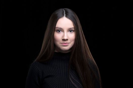 Beautiful girl with dark long hair on a black background. Seventeen-year-old woman. Proper facial features.