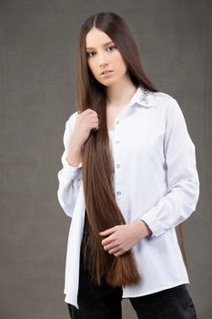 Beautiful young girl with long straight hair in a white shirt posing in the studio on a gray background