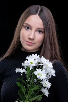 A beautiful young girl with natural beauty with long smooth hair holds a bouquet of white chrysanthemums.