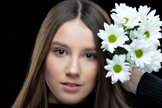 A beautiful young girl with natural beauty with long smooth hair holds a bouquet of white chrysanthemums.