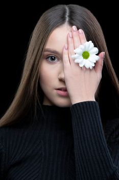 A beautiful girl with natural beauty holds a white flower near her eye. Young girl with a white chrysanthemum.