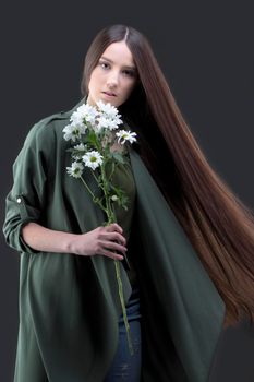 A beautiful young girl with natural beauty with long smooth hair holds a bouquet of white chrysanthemums.