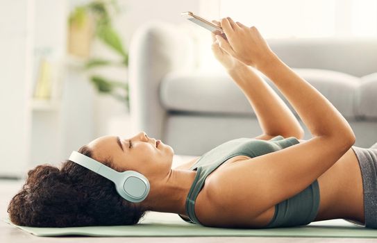 a woman wearing headphones and using her cellphone while wearing workout clothes at home.