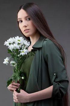 A beautiful young girl with natural beauty with long smooth hair holds a bouquet of white chrysanthemums.