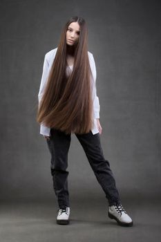 A beautiful girl with very long hair in full growth on a gray background.